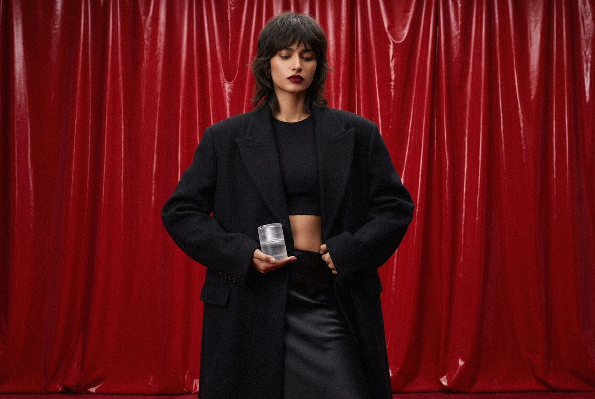 A creator in black holding Bhava in front of red velvet curtains