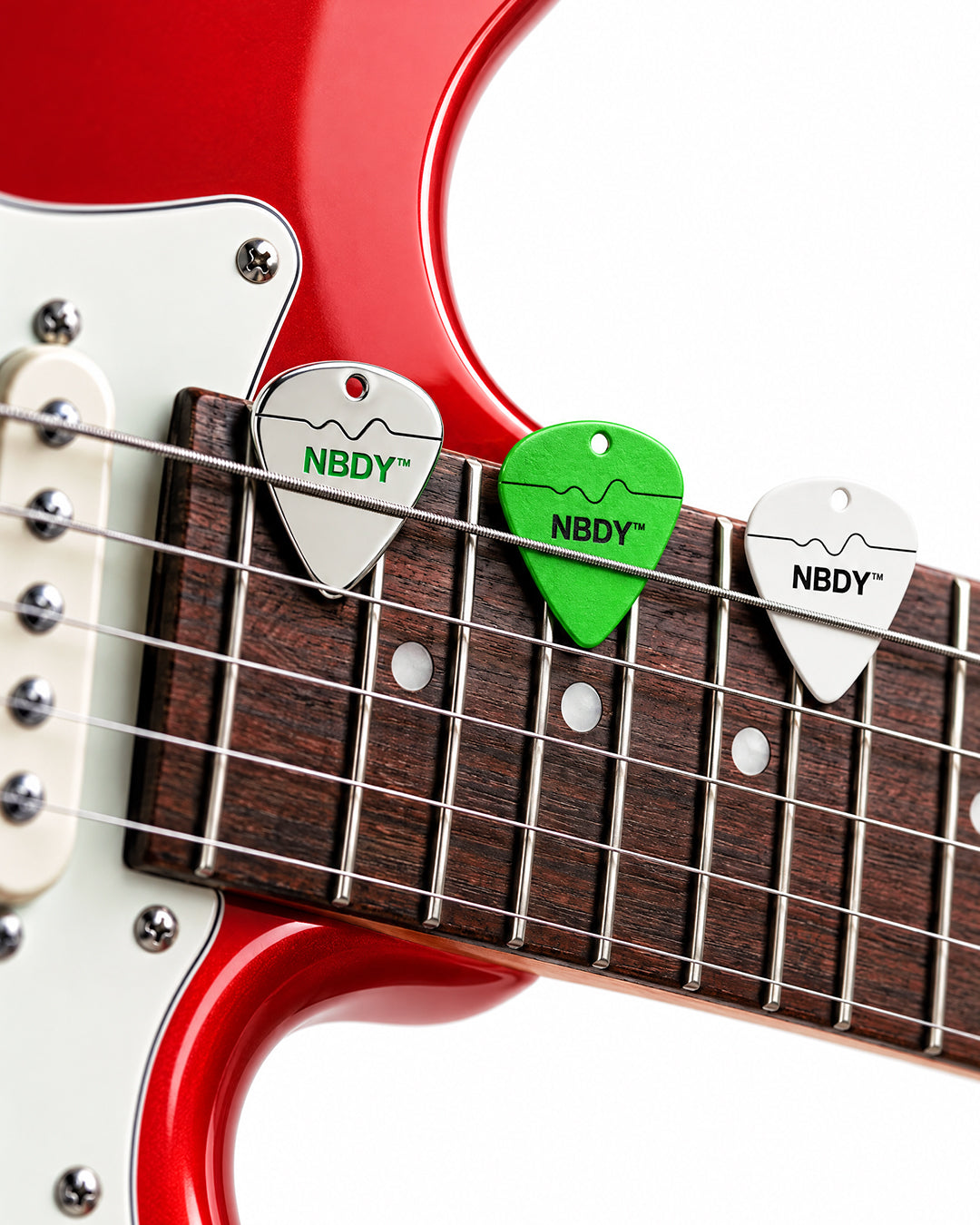 Silver, green and white NBDY picks tucked under the strings of a guitar neck