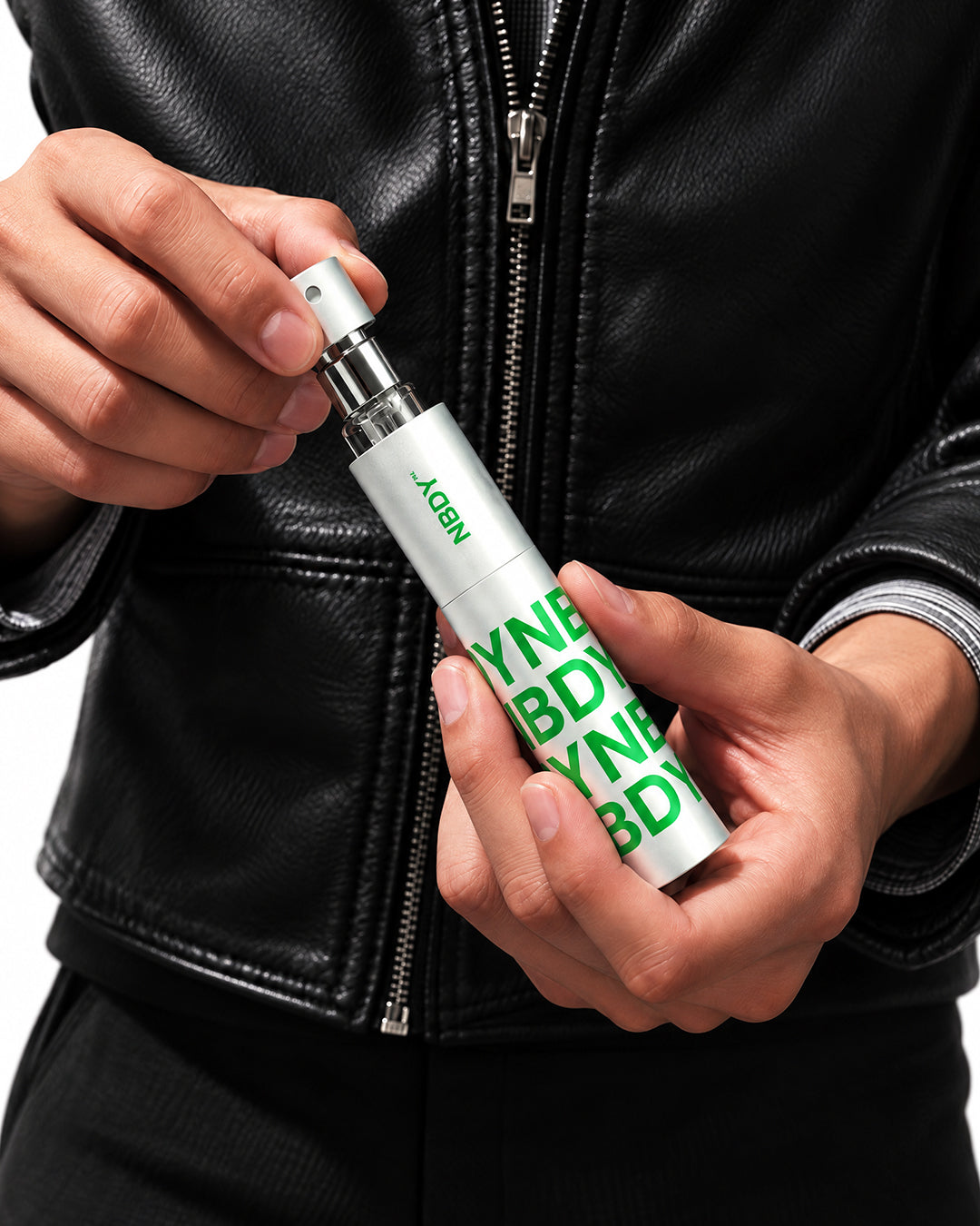 Hands holding the NBDY refillable atomiser against a leather jacket