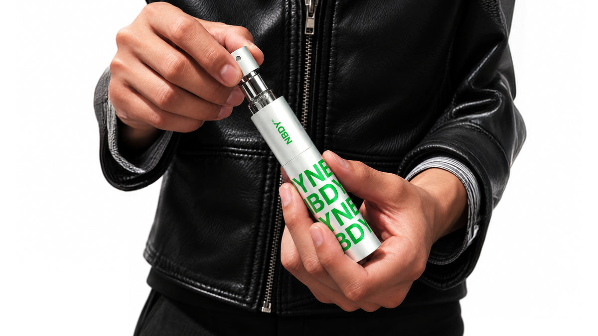 Hands holding the NBDY refillable atomiser against a leather jacket
