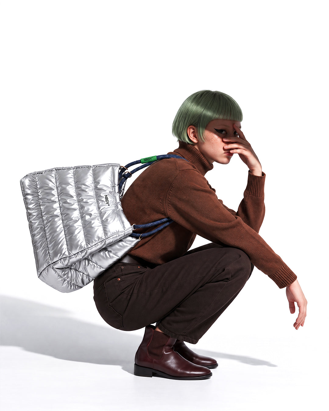 Crouching model with the silver NBDY tote bag on her shoulder