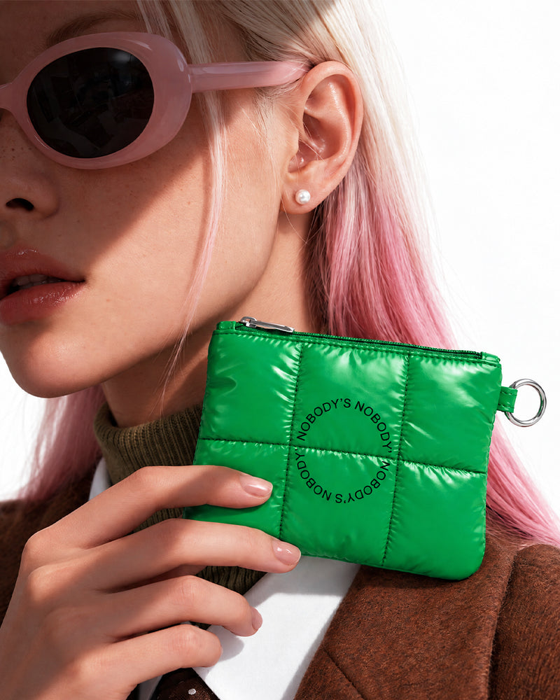Model in pink sunglasses holding the green quilted NOBODY'S NOBODY pouch