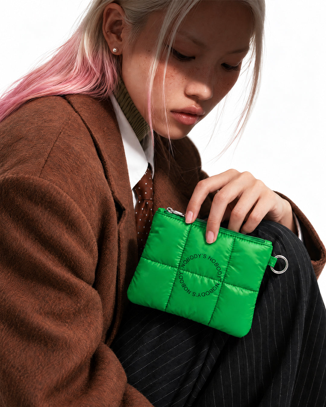 Model in a brown coat holding the green quilted NBDY travel pouch