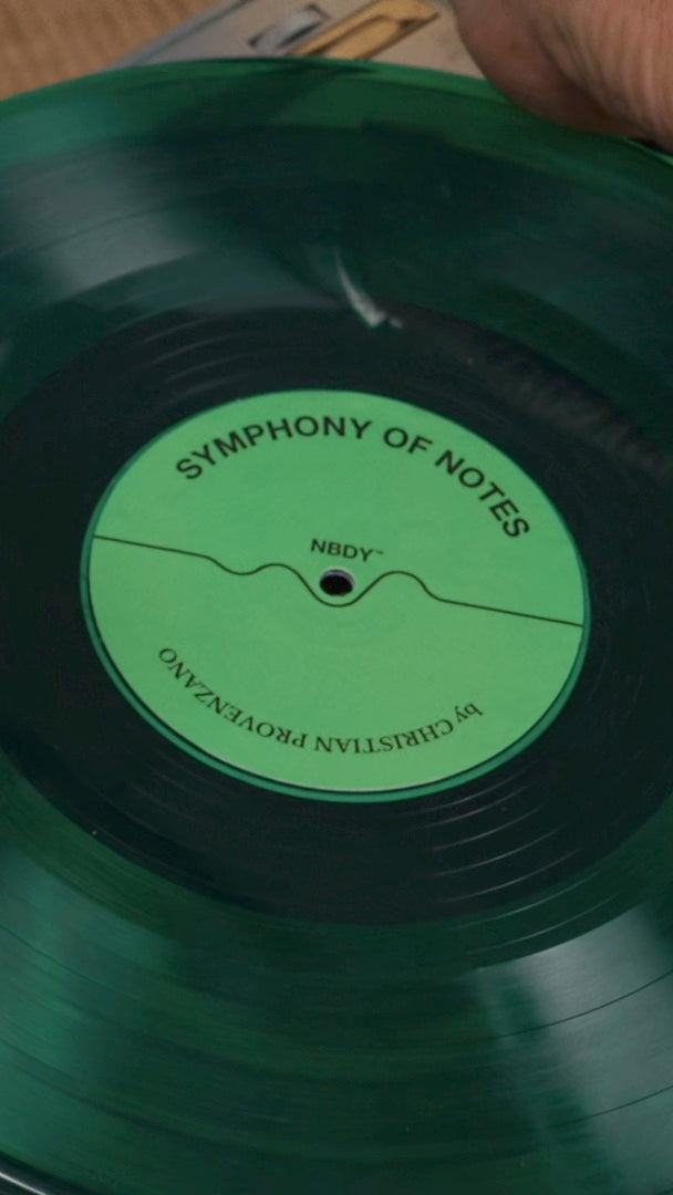 Hands setting the green Symphony of Notes record on a turntable